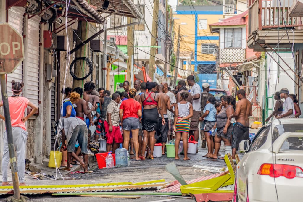 A crowd of people standing close together on the street to fill up water