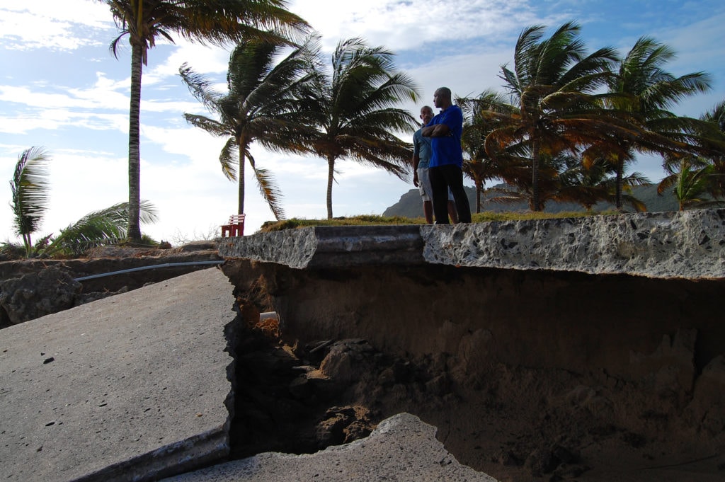 Two men stand at the edge of a washed out concrete road that has been destroyed by soil erosion in St. Lucia.