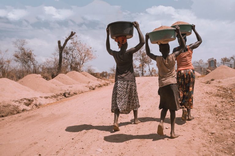 Three women carry containers of soil on their heads.