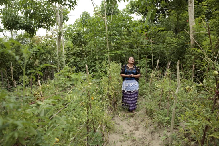 A woman smiles while standing in a vegetable garden.