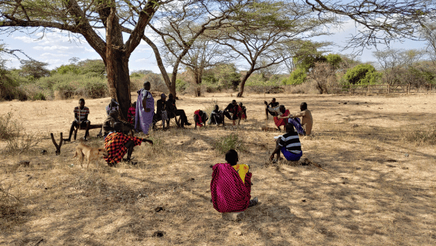People sitting on the floor in a circle next to a tree.