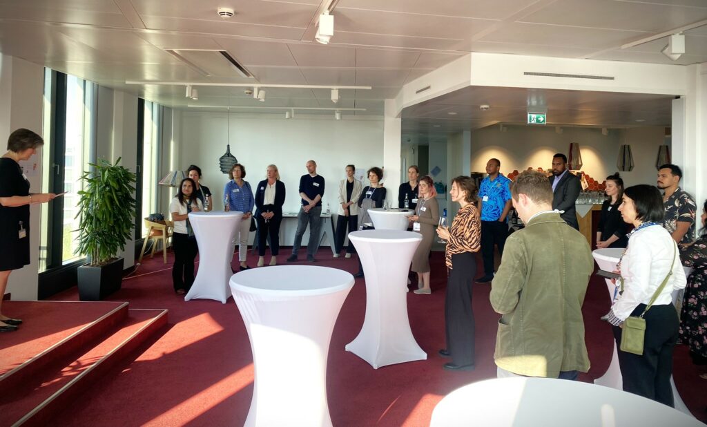 Start of the second phase of the GIZ Global Program with a kick-off event on the topic of human mobility on the campus in Bonn. People are standing in a room with bar tables while someone is giving a speech.