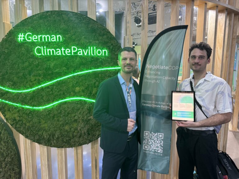 Two men are standing in front of the German Climate Pavilion at COP30, holding an iPad.